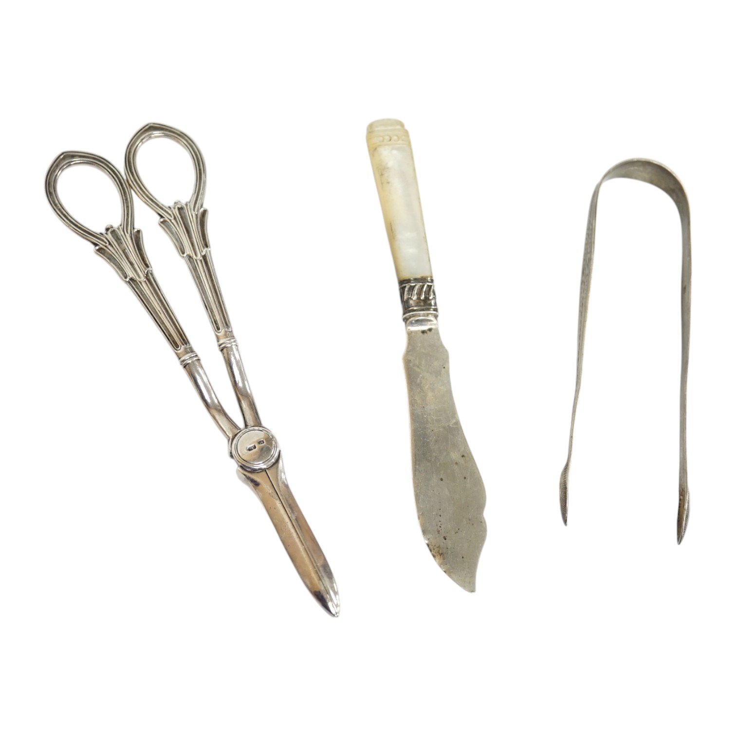 A pair of George V silver grape scissors, Sheffield, 1929, 18.6cm, together with a mother of pearl handled silver butter knife ad a pair of Georgian silver sugar tongs by Peter & Ann Bateman. Condition - poor to fair